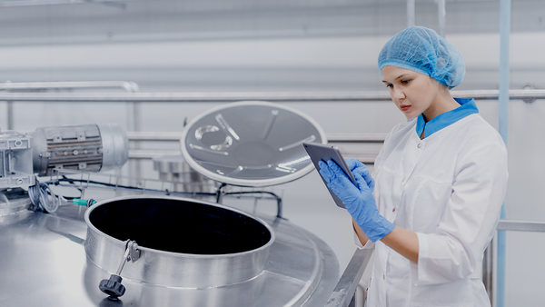 Ein Arbeiter kontrolliert mit Hilfe eines Tablets Stahltanks mit Milch aus einer modernen industriellen Produktion